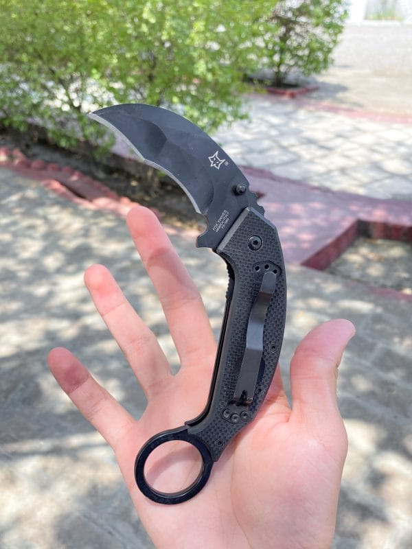 Black folding karambit knife with curved blade and finger ring for tactical use