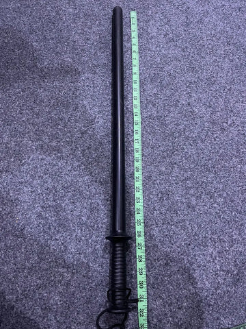 Black polymer security baton with textured grip and wrist strap next to measuring tape