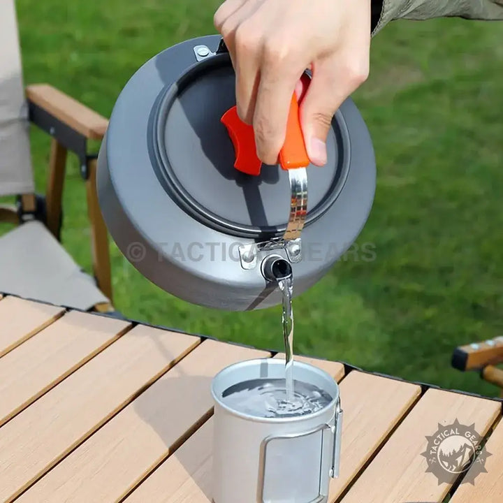 Lightweight camping kettle with orange heat-resistant handle pouring water into a metal cup in Aluminum 12PCS Camping Cooking Set