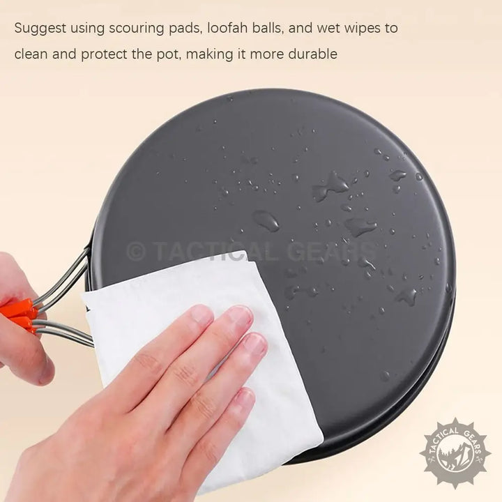 Dark non-stick cooking pot with foldable orange handles from Aluminum 12PCS Camping Cooking Set being wiped clean, ideal for camping frying pan use