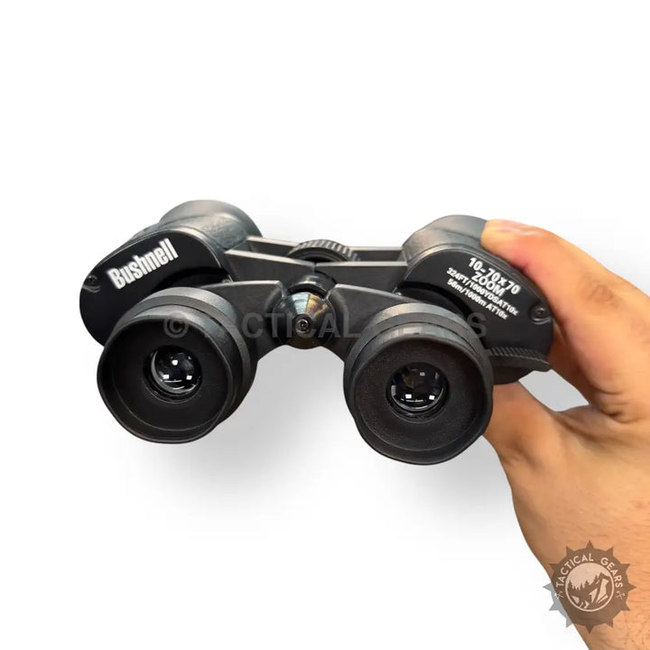 Black Bushnell 70x70 zooming binoculars held in hand for clear long-distance viewing