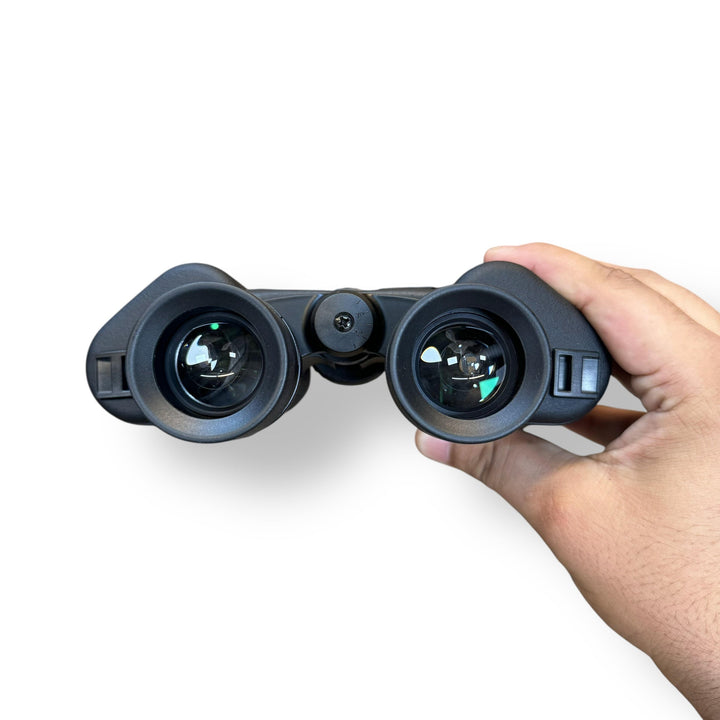 Black binoculars with green-tinted lenses held by hand, featuring diopter adjustment in Comet 7x50