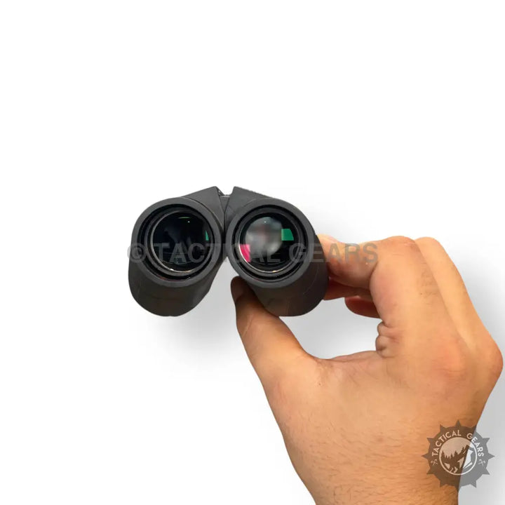 Black 20x25 mini binocular with green and red lens reflections held in hand