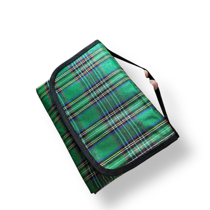Foldable green plaid picnic sheet with black trim and carrying strap, ideal for person picnic sheet use