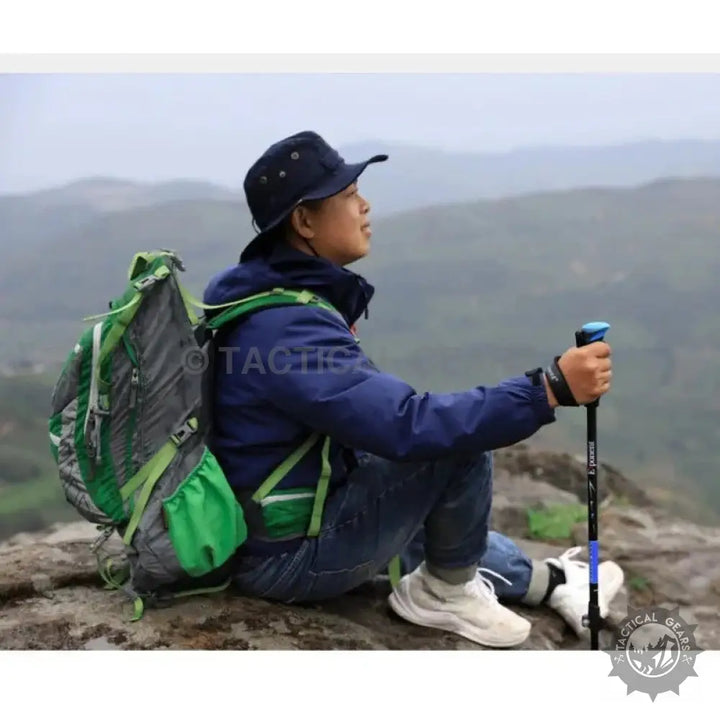 Person sitting with a blue trekking stick, wearing a hat, jeans, and backpack