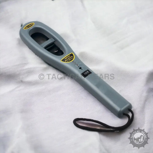 Gray handheld metal detector with wrist strap featuring red indication light for security detection