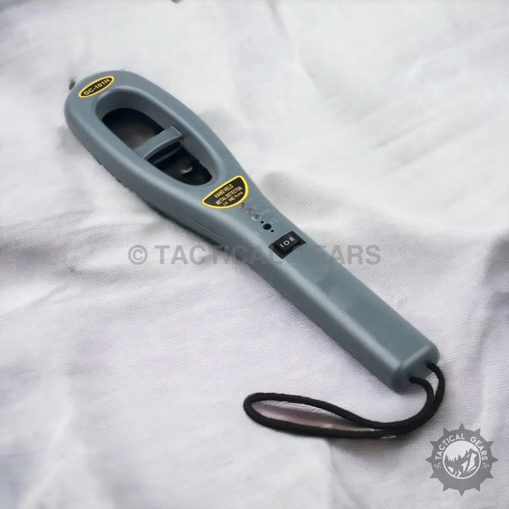 Gray handheld metal detector with wrist strap featuring red indication light for security detection