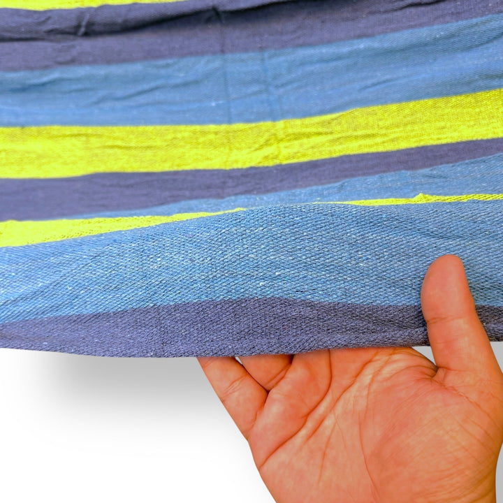 Hand holding a blue, purple, and yellow striped imported hammock fabric with green stripes