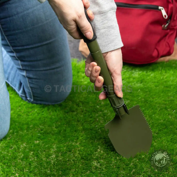 Person holding a dark green portable camping shovel with serrated edge