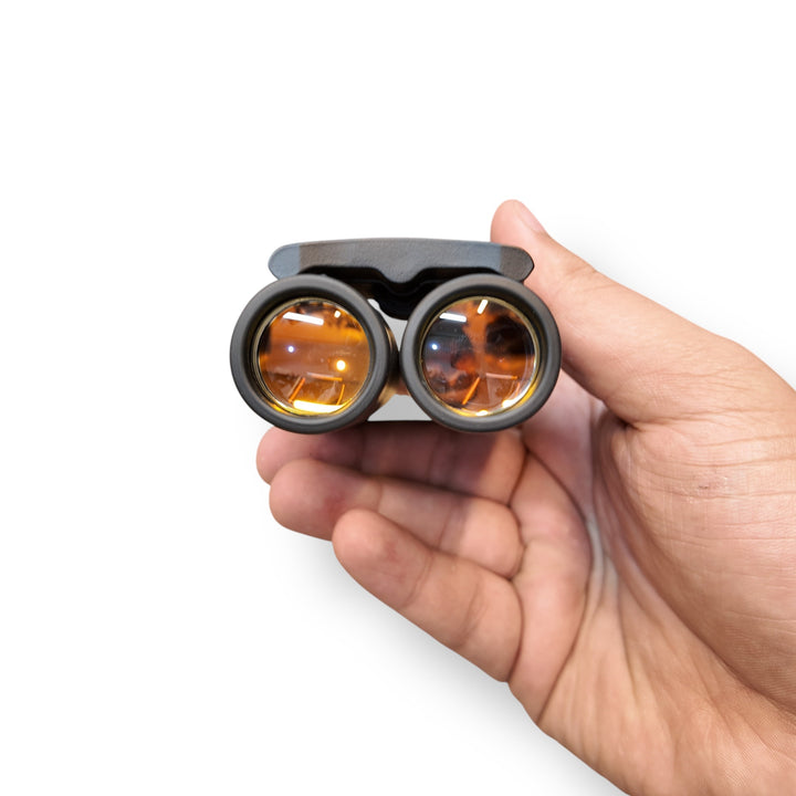 Pocket size mini binoculars with black frame and orange-tinted lenses in hand