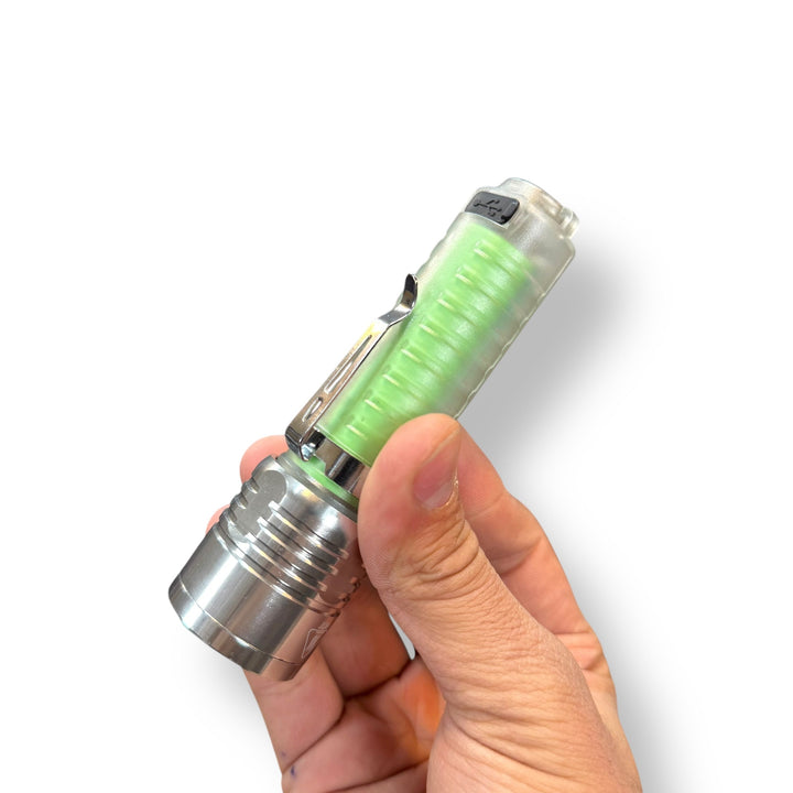 Hand holding a USB rechargeable flashlight with clear body, green battery, and metal head