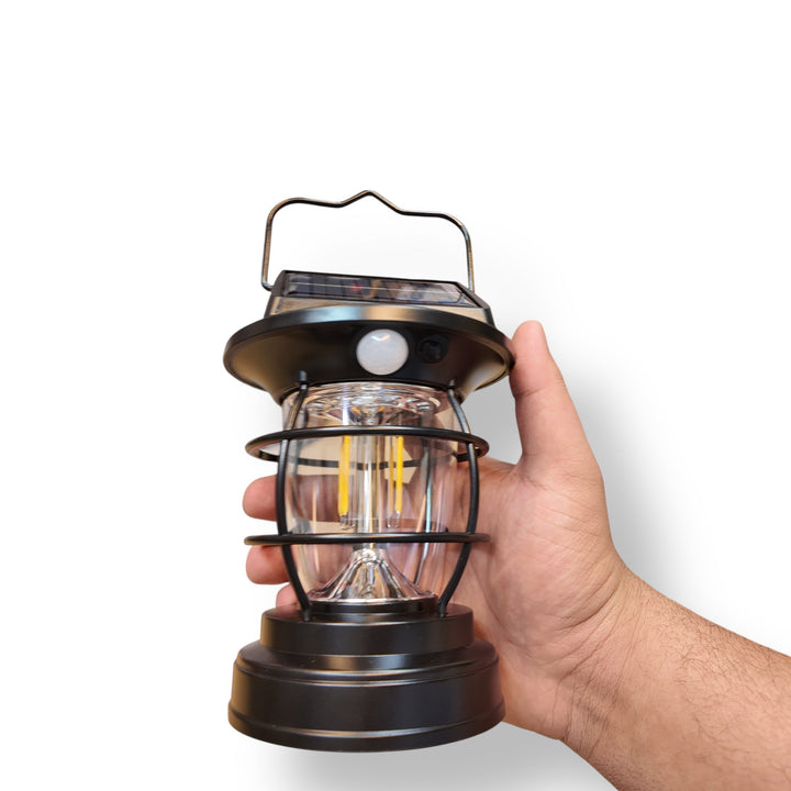 Black lantern solar sensor lamp held in hand with clear glass globe and LED bulbs