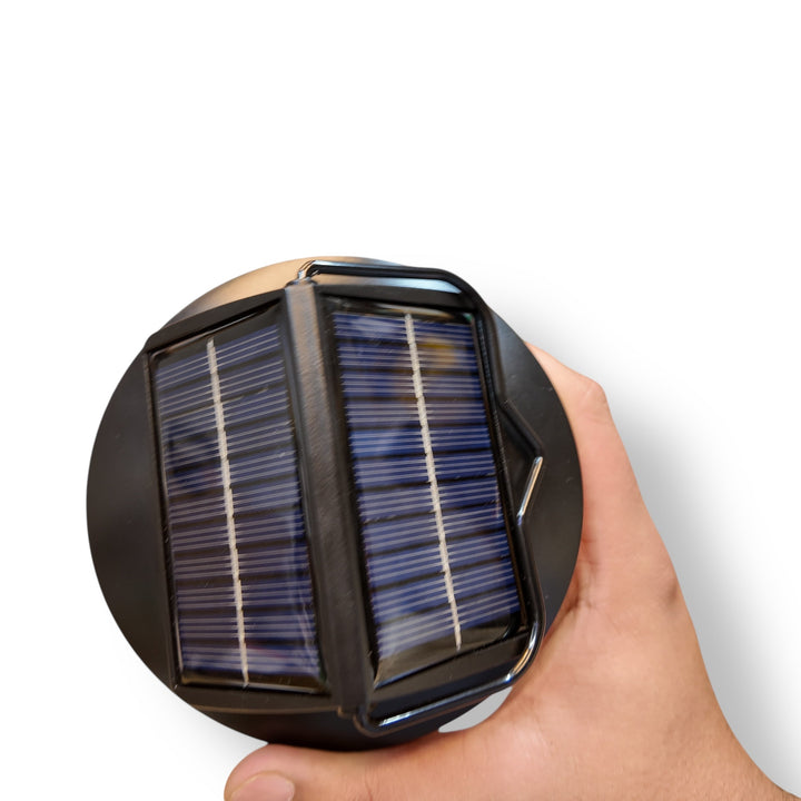 Hand holding a compact solar sensor lamp with round solar panel and photovoltaic cells