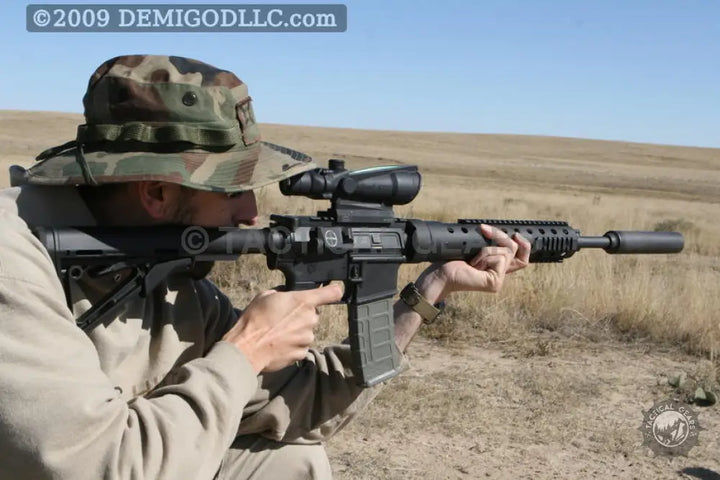Person aiming with a camouflage boonie hat using a Trijicon tactical red dot sight