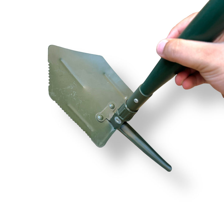 Person holding a dark green USA Tactical Folding Shovel with serrated edge