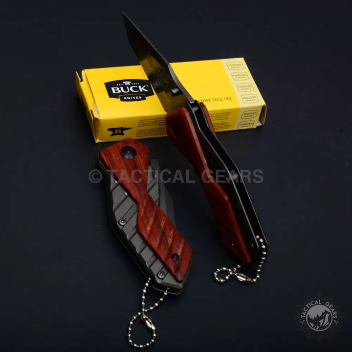 Two Buck USA X59 Tactical Mini Folding Knives with reddish-brown wood handles near a yellow Buck Knives box