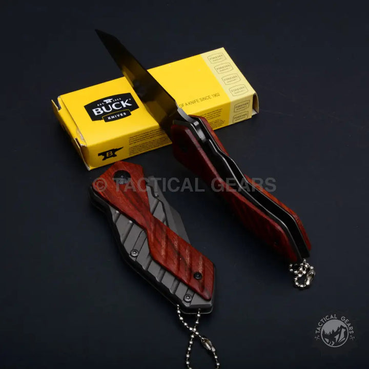 Two tactical folding knives with dark red wooden handles and silver keychains near Buck USA X59 Tactical box